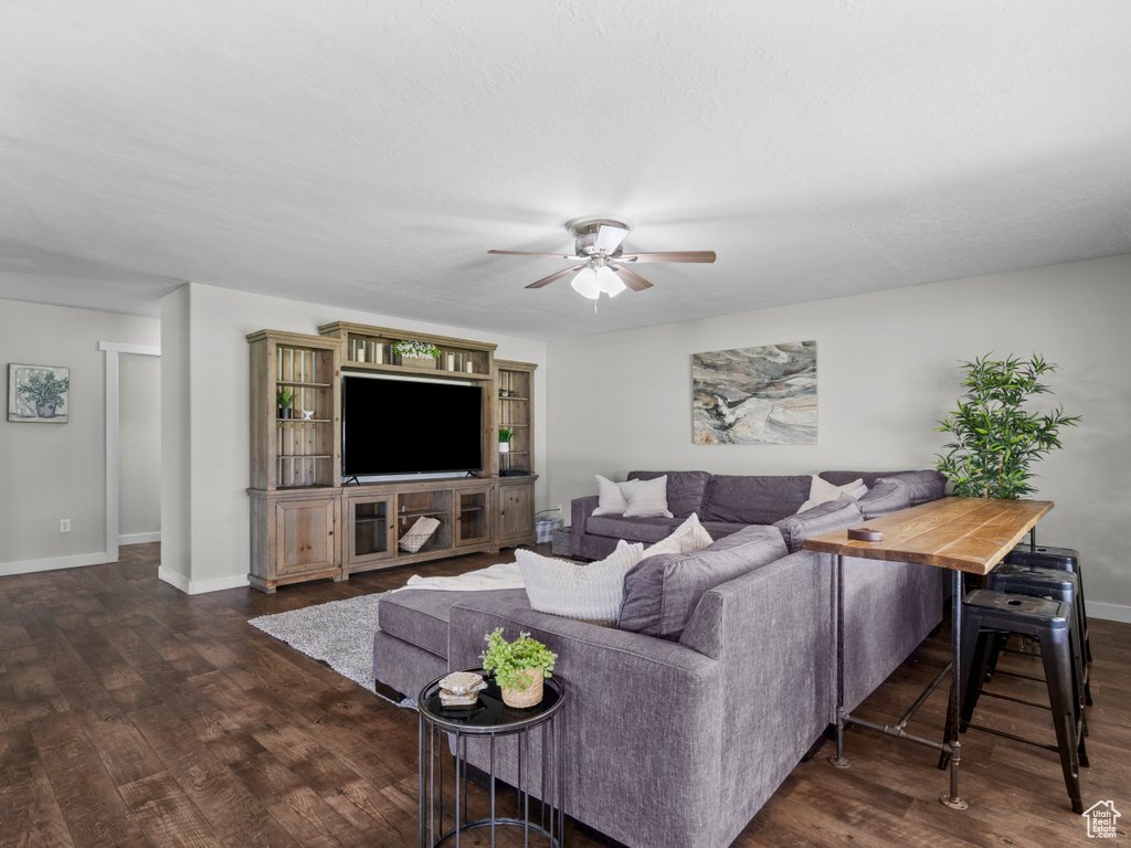 Living room featuring dark wood-style floors, a ceiling fan, and baseboards