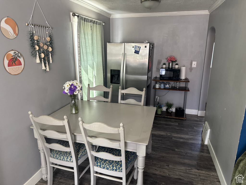 Dining area with dark wood-style flooring, crown molding, baseboards, arched walkways, and a textured ceiling