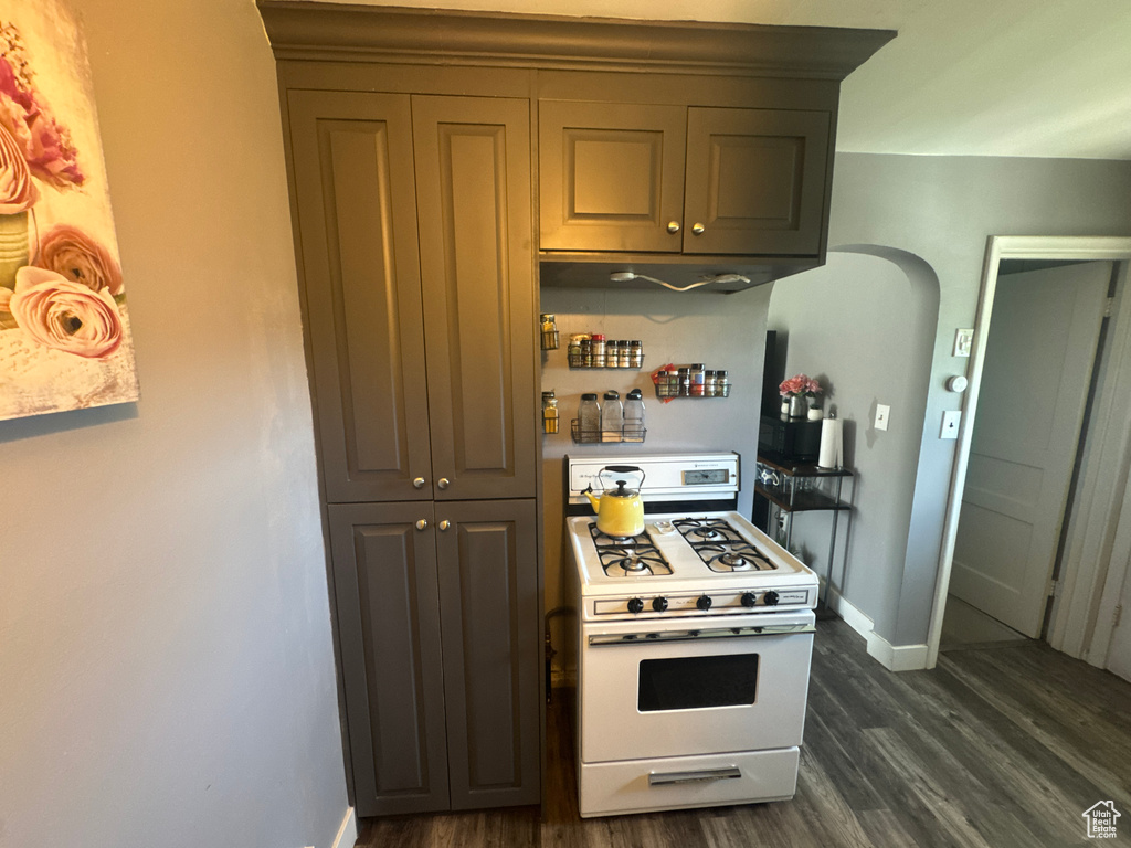 Kitchen with white gas stove, dark wood finished floors, baseboards, and arched walkways