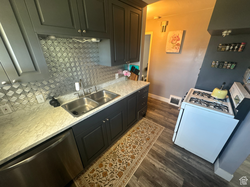 Kitchen featuring white range with gas stovetop, stainless steel dishwasher, a sink, dark wood finished floors, and light countertops