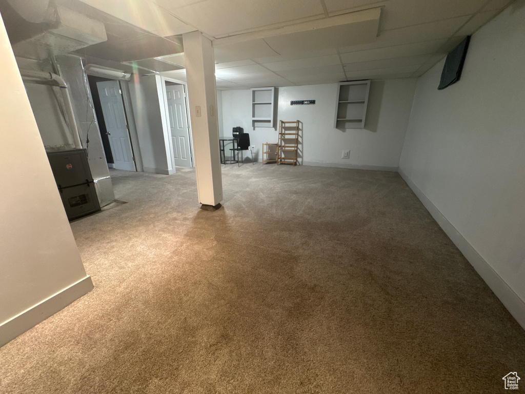 Finished below grade area with carpet flooring, baseboards, a drop ceiling, and heating unit