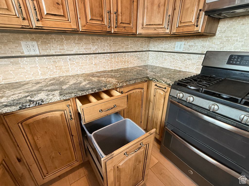 Kitchen with range with two ovens, backsplash, brown cabinetry, and dark stone counters