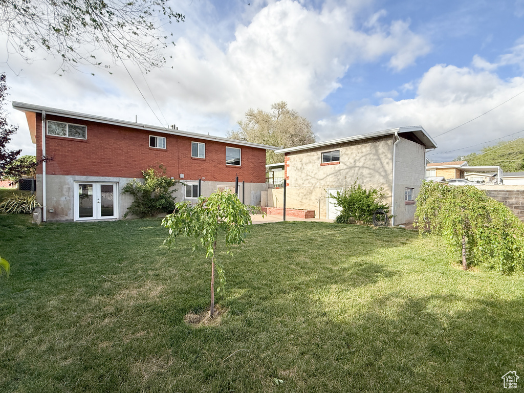 Back of house featuring french doors, a lawn, and brick siding