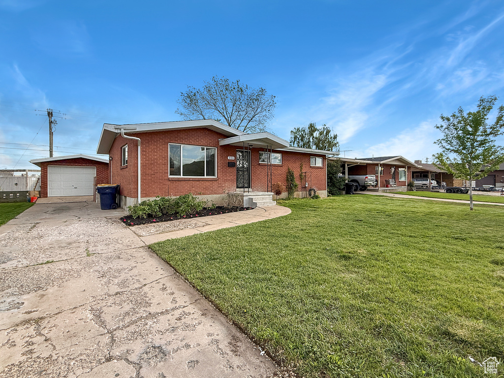 Ranch-style home with brick siding, concrete driveway, a front yard, and an outdoor structure
