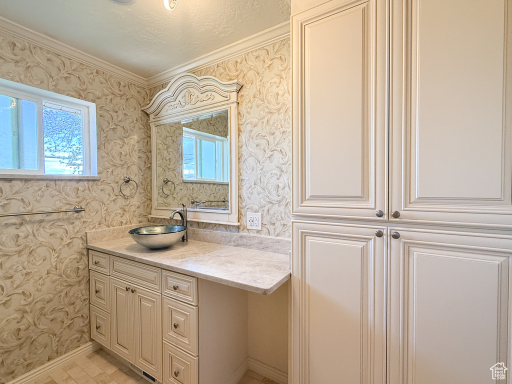 Bathroom featuring wallpapered walls, vanity, crown molding, and baseboards