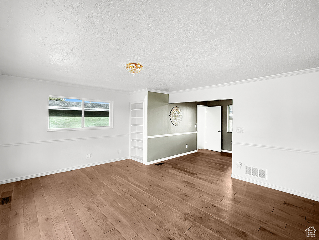 Unfurnished room with a textured ceiling, wood finished floors, ornamental molding, and baseboards