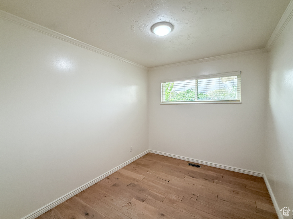 Unfurnished room featuring light wood-style floors, crown molding, and baseboards