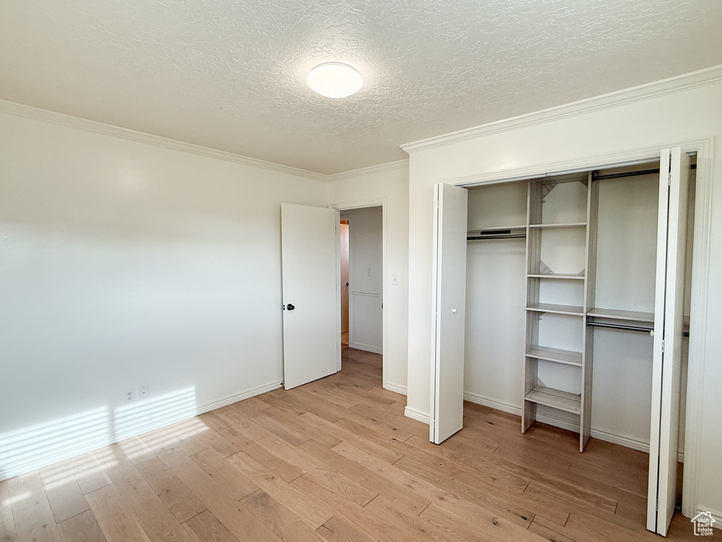 Unfurnished bedroom with ornamental molding, light wood finished floors, a textured ceiling, a closet, and baseboards