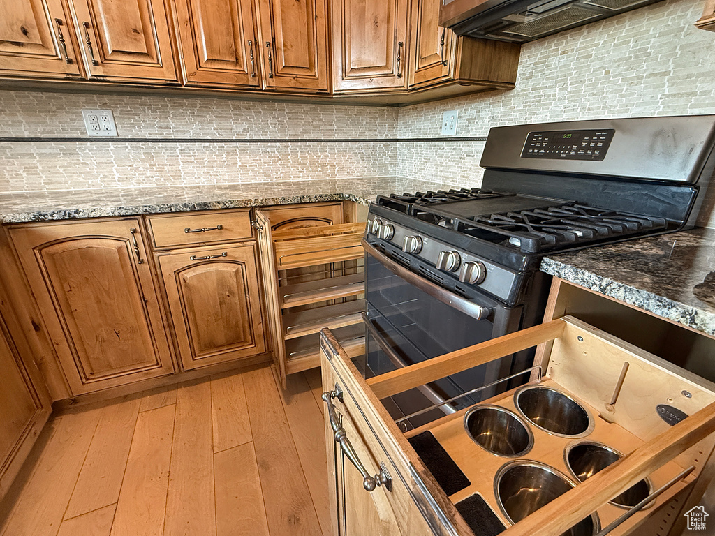 Kitchen with gas range, tasteful backsplash, brown cabinetry, and light stone countertops