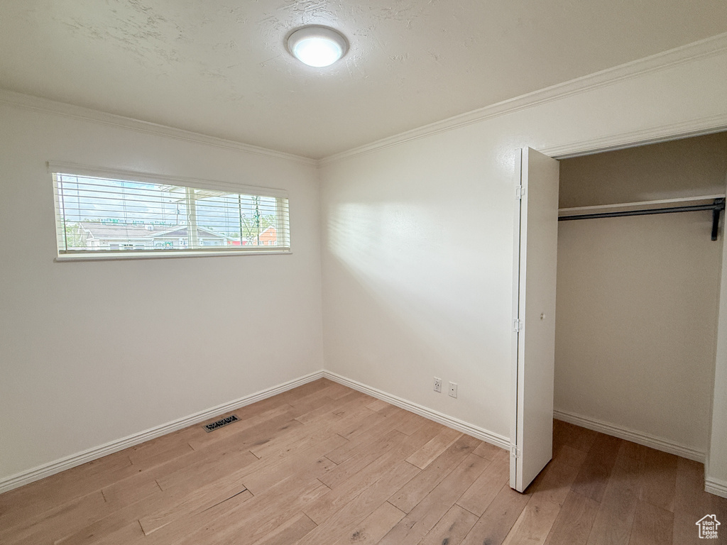 Unfurnished bedroom with light wood finished floors, a closet, ornamental molding, and baseboards