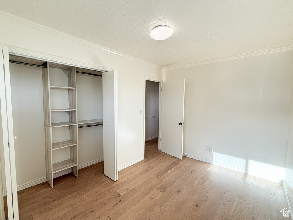 Unfurnished bedroom featuring ornamental molding, light wood-type flooring, a closet, and baseboards