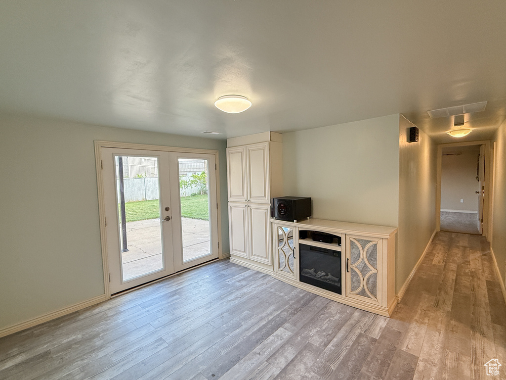 Unfurnished living room with light wood-type flooring, french doors, baseboards, and a glass covered fireplace
