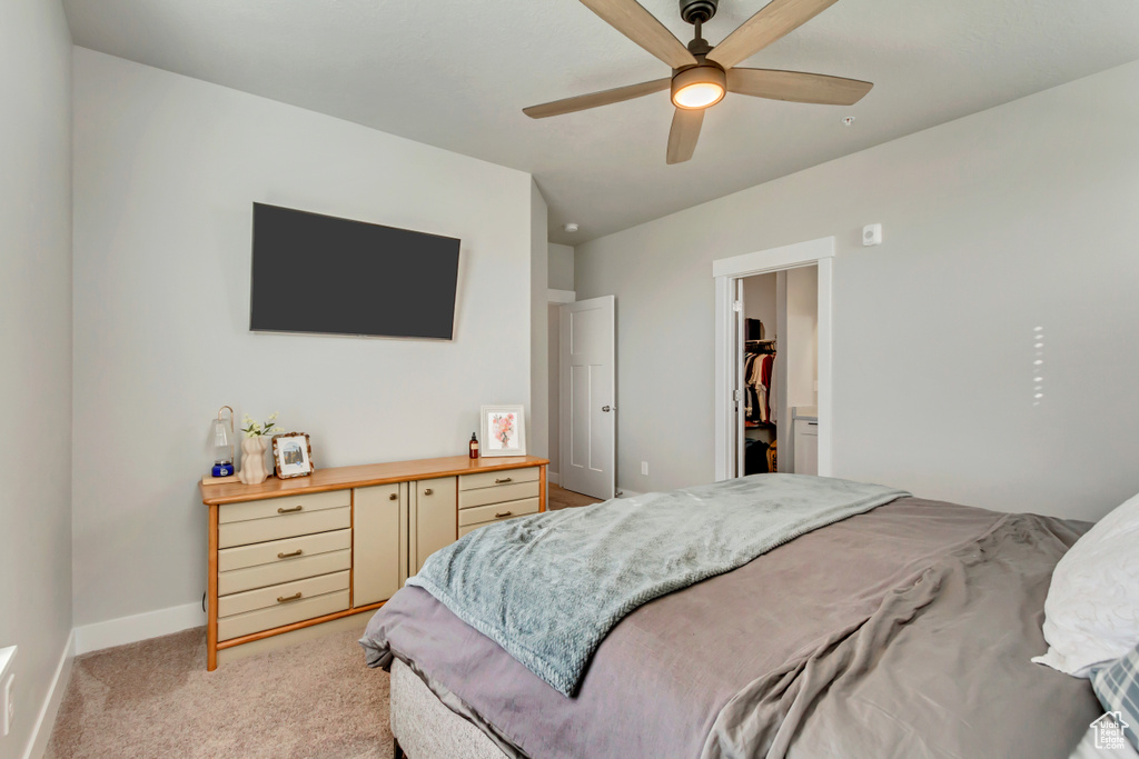 Bedroom featuring light colored carpet, a walk in closet, baseboards, and a ceiling fan