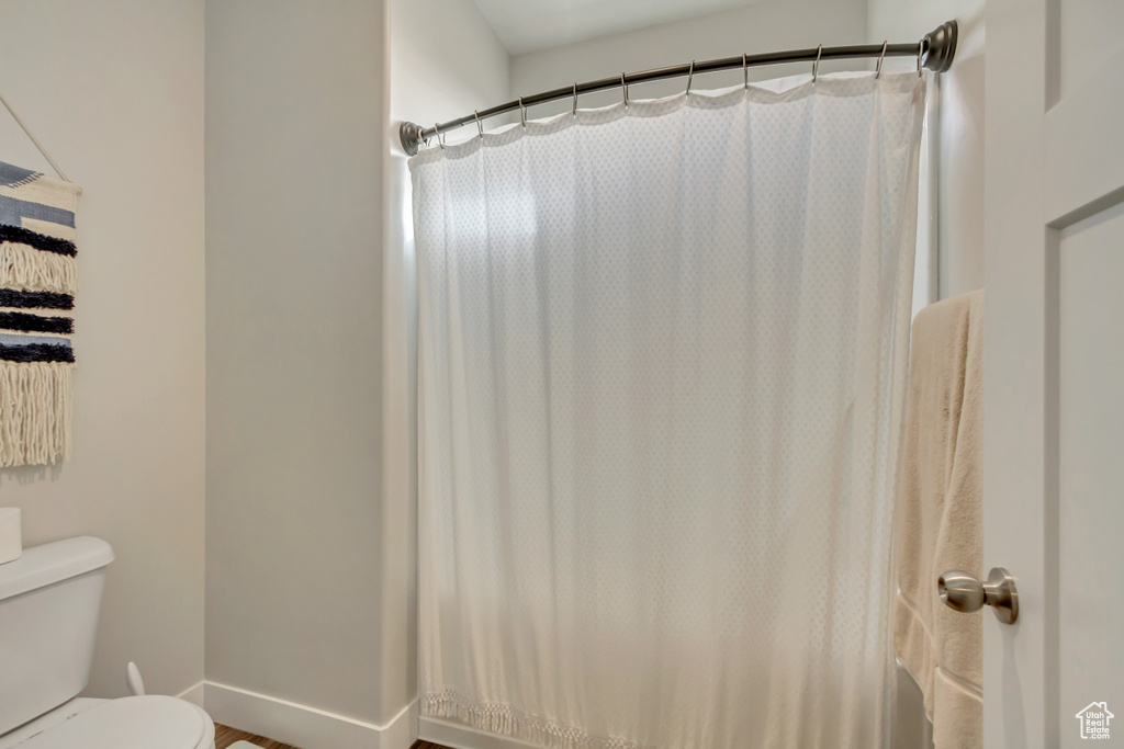 Bathroom featuring toilet, a shower with shower curtain, and baseboards