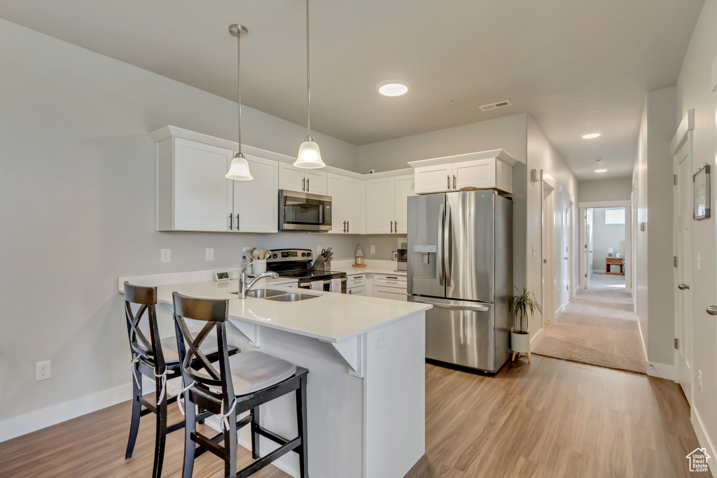 Kitchen with appliances with stainless steel finishes, a sink, a peninsula, light wood finished floors, and light countertops