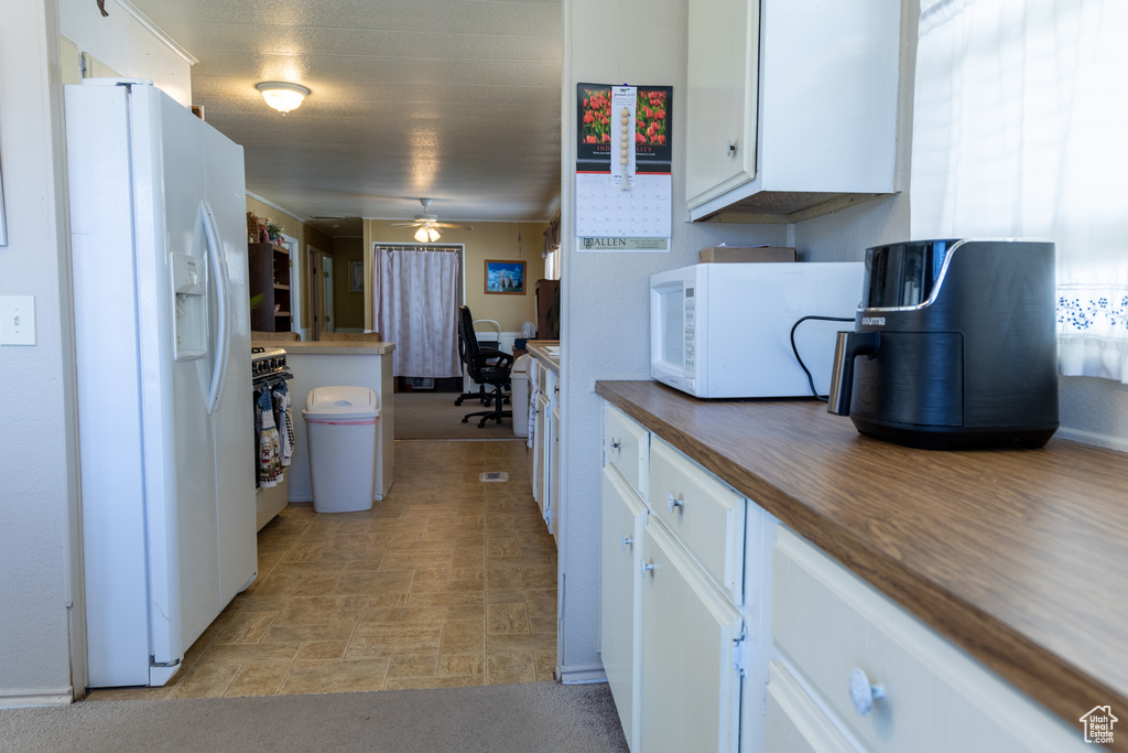 Kitchen with white appliances, white cabinetry, a ceiling fan, and dark countertops
