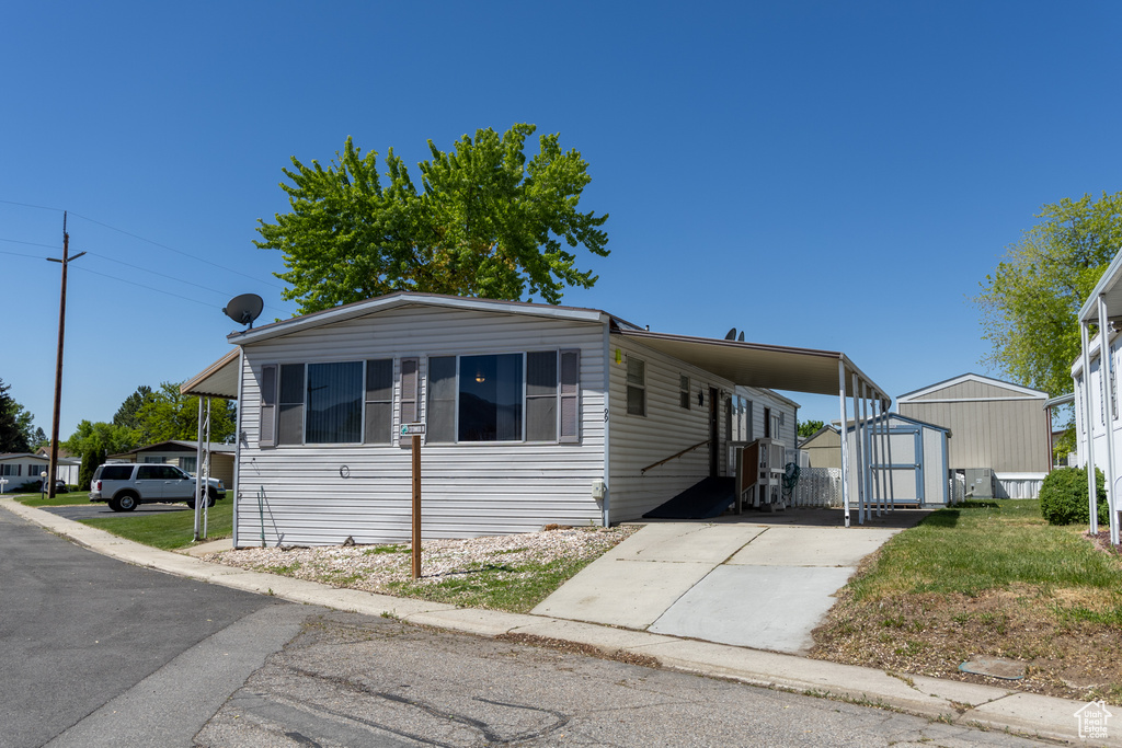 Manufactured / mobile home with a storage unit, concrete driveway, an outbuilding, and a carport