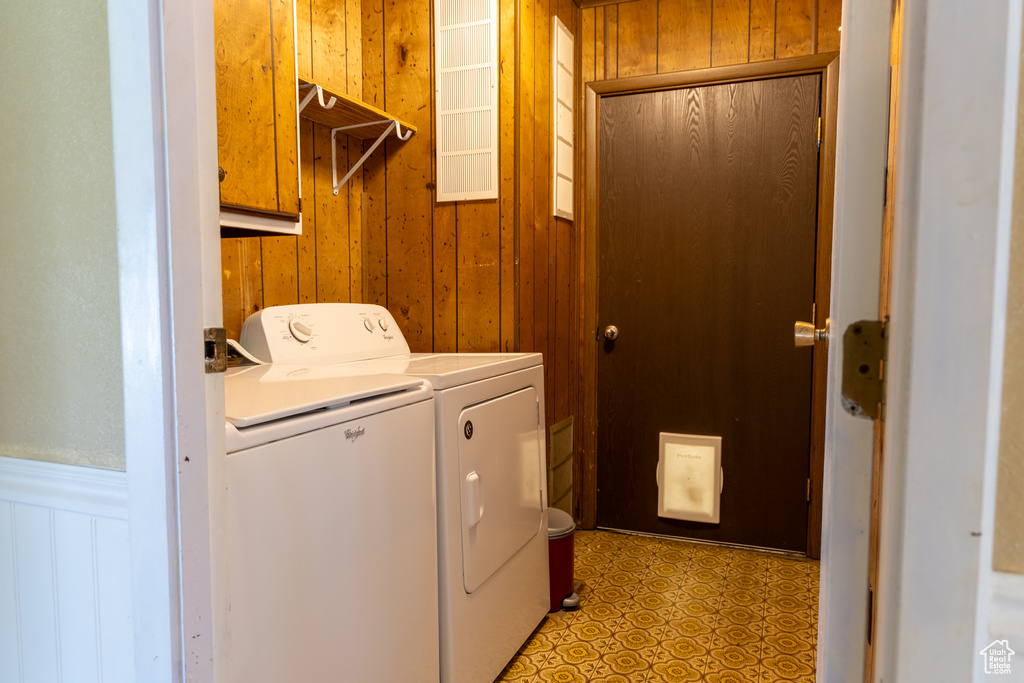 Clothes washing area with washer and clothes dryer, cabinet space, wood walls, a wainscoted wall, and light floors