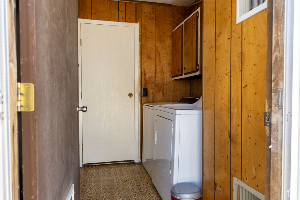 Clothes washing area with cabinet space, wood walls, and washing machine and clothes dryer