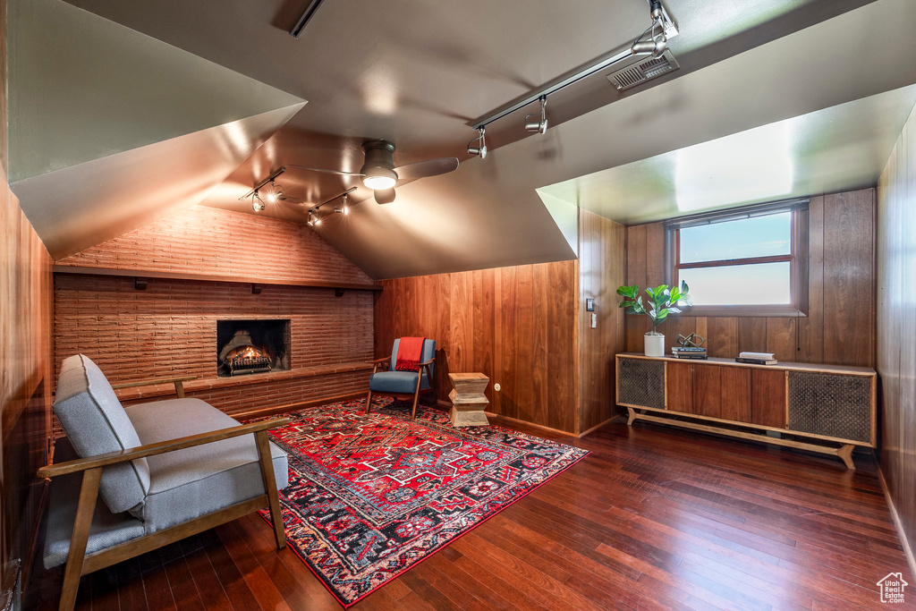 Living area with rail lighting, wooden walls, hardwood / wood-style flooring, lofted ceiling, and a ceiling fan