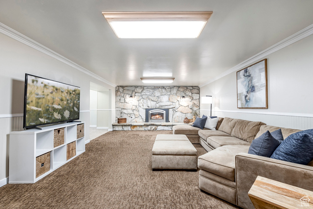 Living room with ornamental molding, a stone fireplace, and carpet floors
