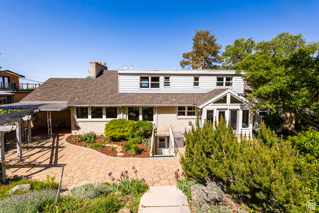 Rear view of property featuring brick siding, a patio, a chimney, and a shingled roof