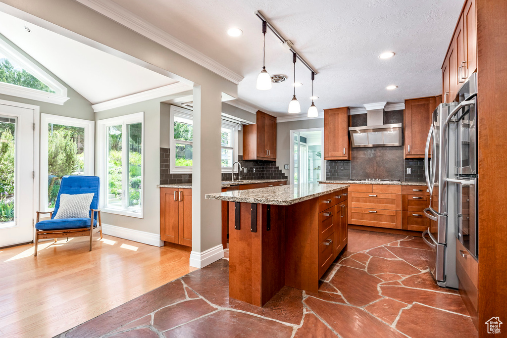 Kitchen featuring brown cabinetry, ornamental molding, tasteful backsplash, a center island, and a sink