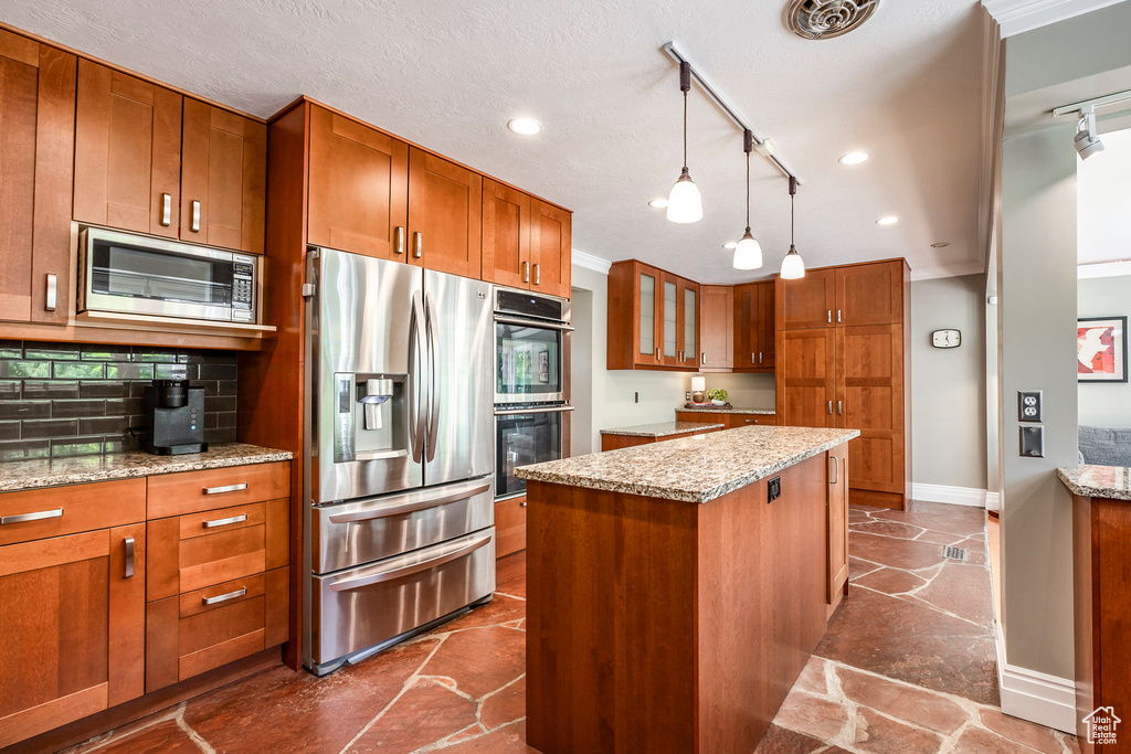 Kitchen with stainless steel appliances, rail lighting, brown cabinetry, baseboards, and a kitchen island