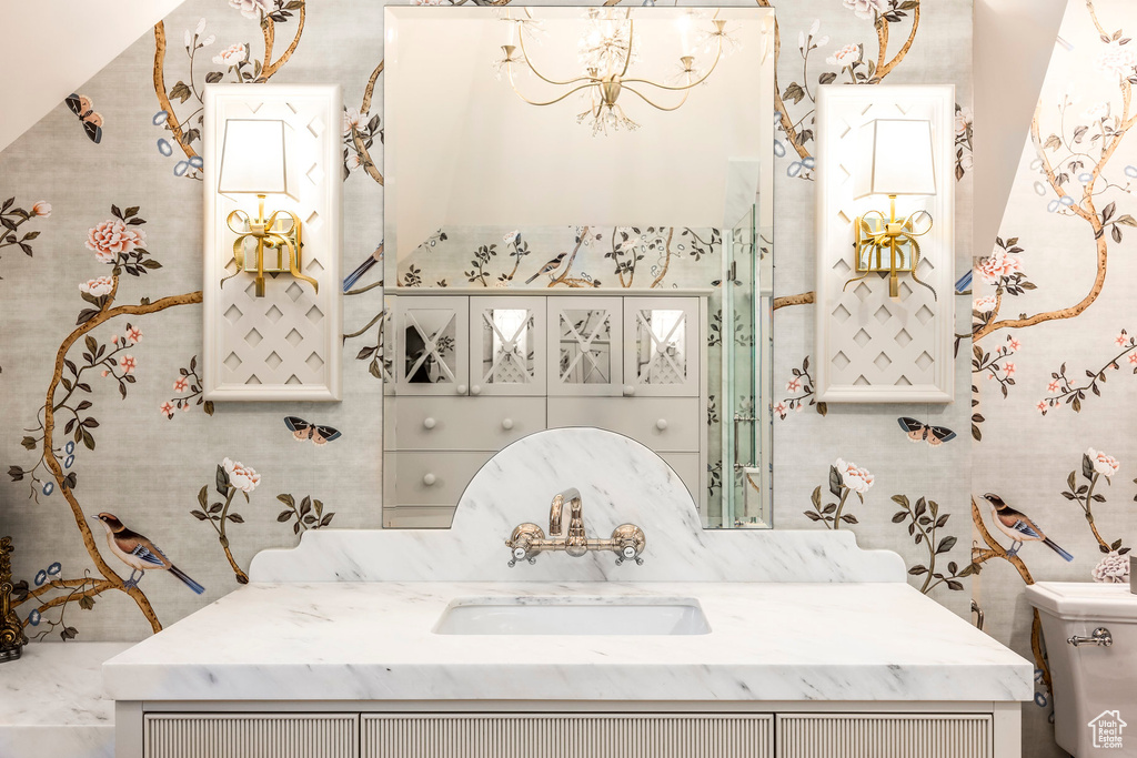 Bathroom with a chandelier, vanity, toilet, and wallpapered walls