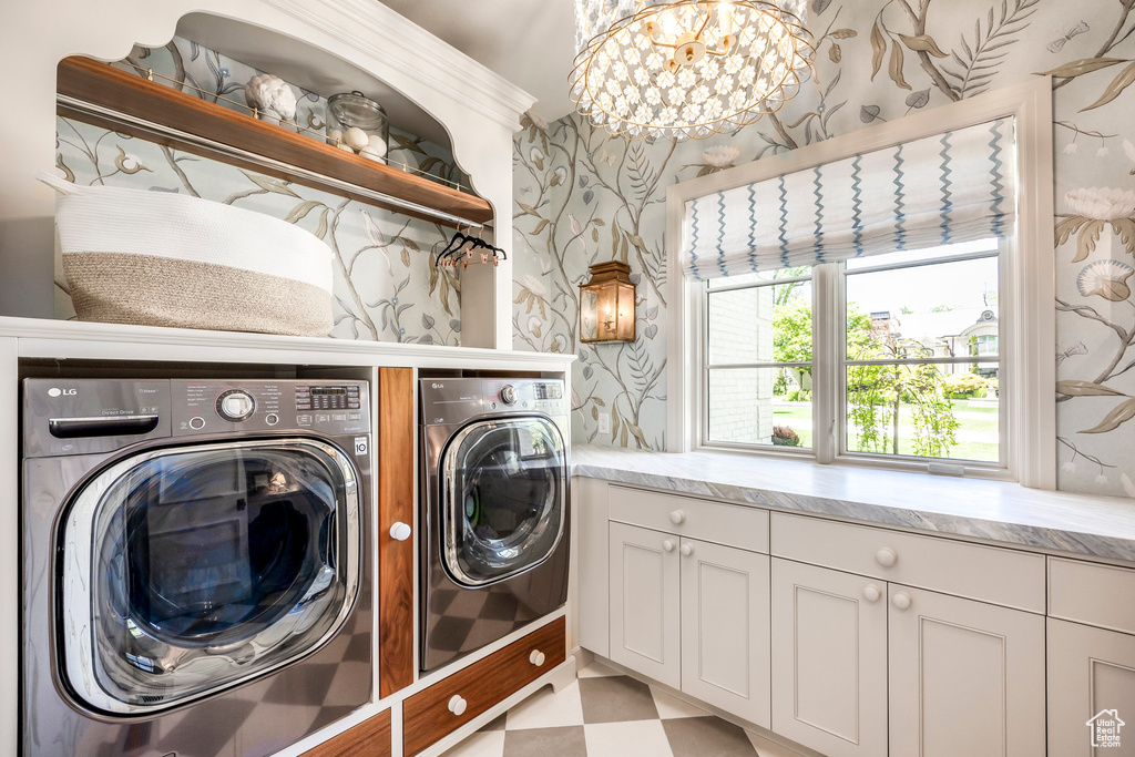 Laundry room featuring separate washer and dryer, wallpapered walls, cabinet space, light floors, and a chandelier
