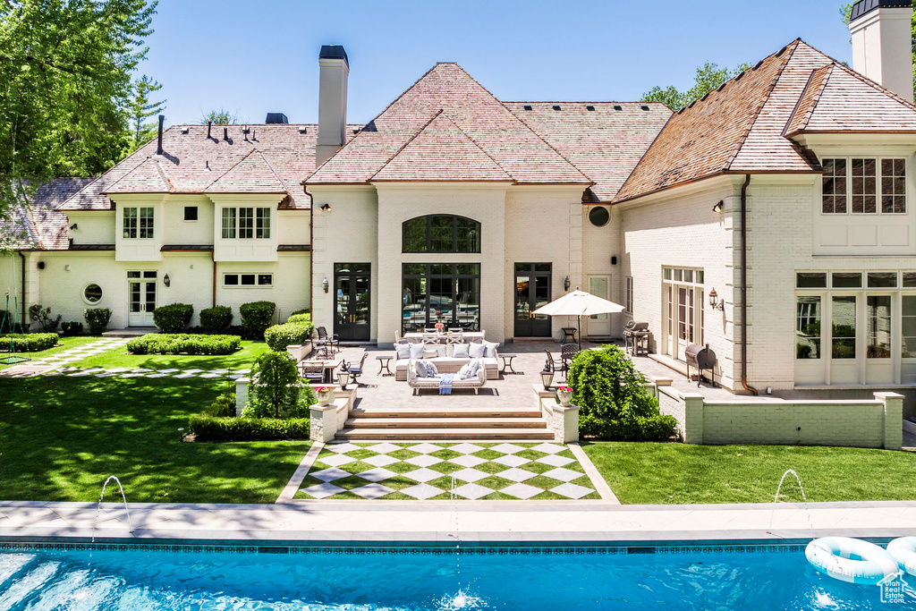 Back of house featuring a chimney, a high end roof, french doors, and an outdoor pool