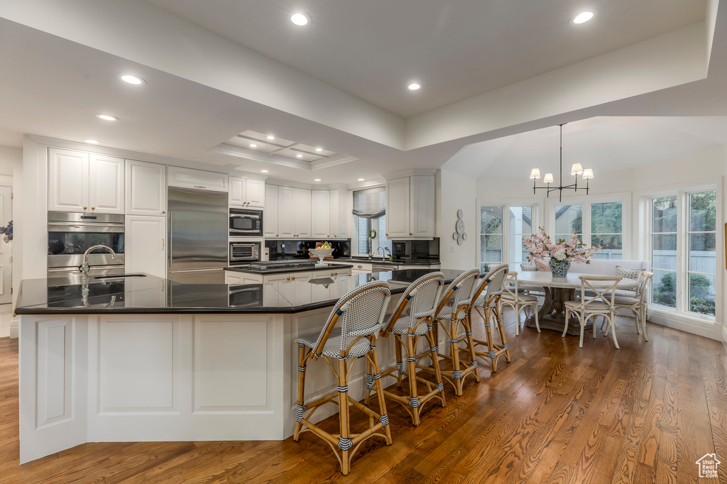 Kitchen with built in appliances, dark countertops, dark wood-type flooring, a chandelier, and recessed lighting