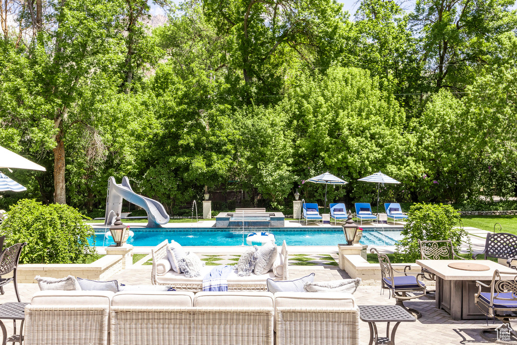Swimming pool with a water slide, an outdoor living space, a patio, and view of wooded area