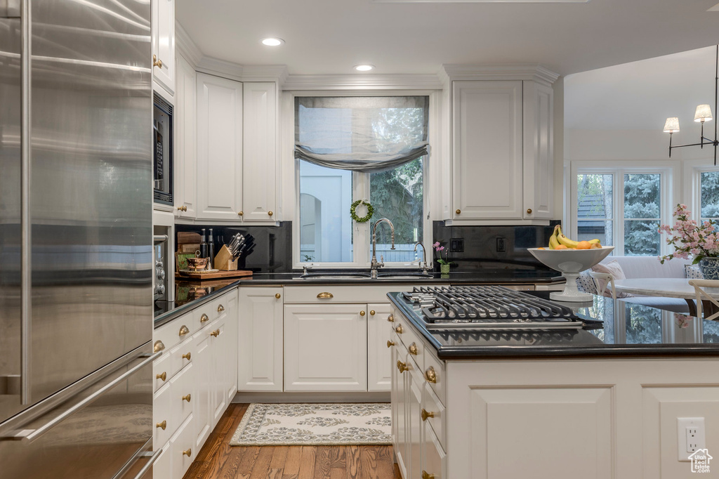 Kitchen featuring built in appliances, a sink, dark countertops, wood finished floors, and white cabinetry