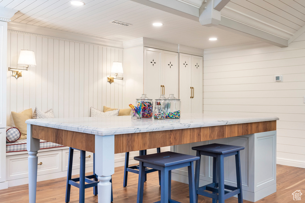 Kitchen featuring a kitchen bar, light wood finished floors, wood walls, recessed lighting, and white cabinetry