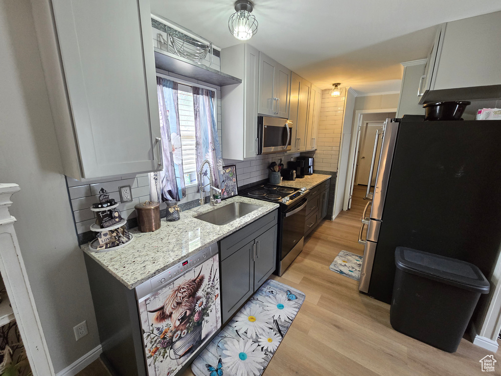 Kitchen featuring appliances with stainless steel finishes, a sink, tasteful backsplash, light wood finished floors, and light stone counters