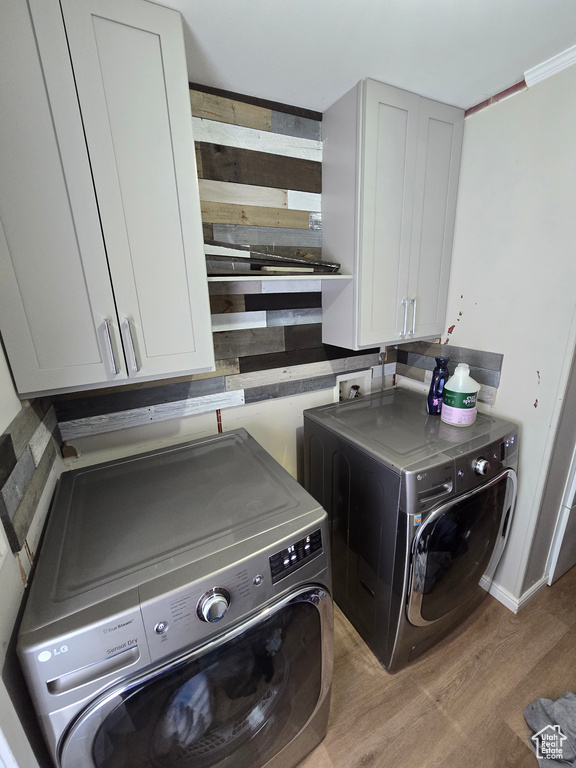 Clothes washing area with washer and dryer, cabinet space, and light wood-style flooring
