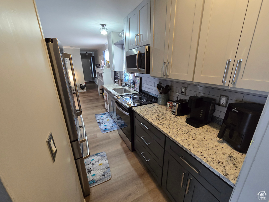 Kitchen with stainless steel appliances, light wood-style floors, tasteful backsplash, and a sink