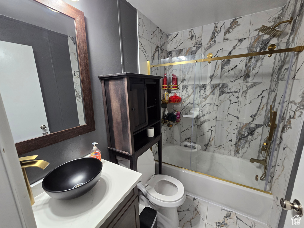 Bathroom featuring combined bath / shower with glass door, marble look tiles, vanity, and toilet