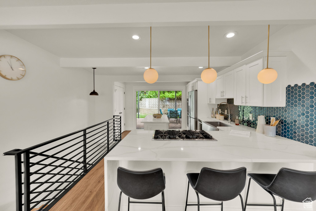Kitchen featuring a sink, stainless steel appliances, a peninsula, light stone counters, and white cabinetry