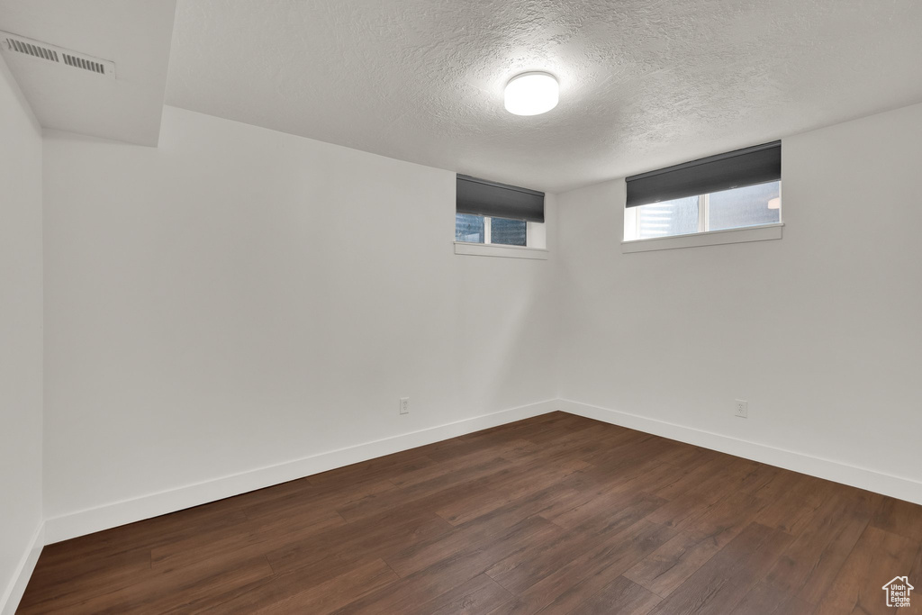 Basement with dark wood-style flooring, a textured ceiling, and baseboards