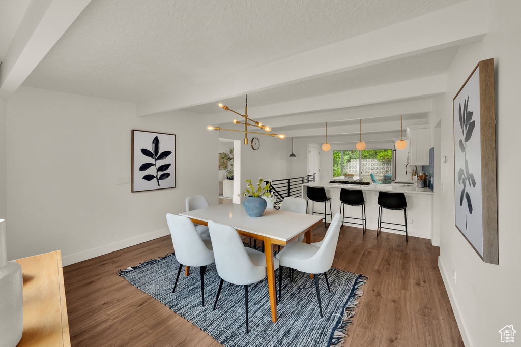 Dining room featuring baseboards, wood finished floors, beam ceiling, a chandelier, and a textured ceiling