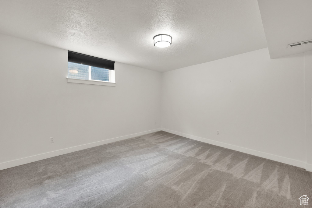Carpeted empty room featuring a textured ceiling and baseboards