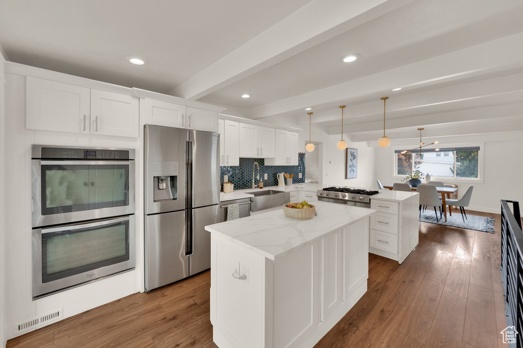 Kitchen with stainless steel appliances, a peninsula, beamed ceiling, a kitchen island, and dark wood-type flooring