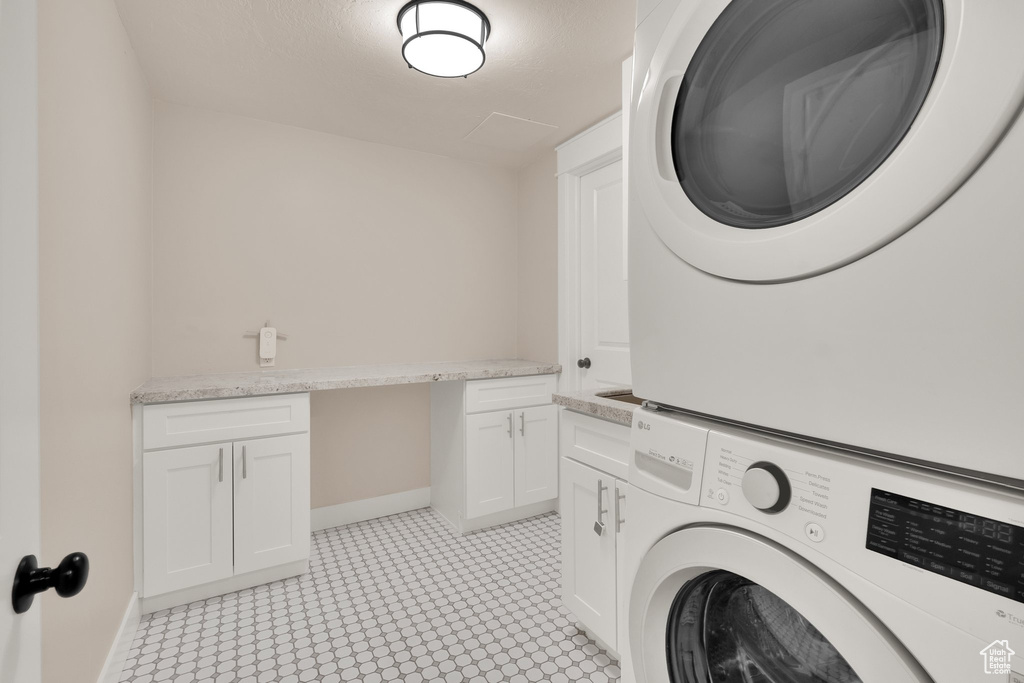 Laundry room with estacked washer and dryer, cabinet space, baseboards, and light flooring