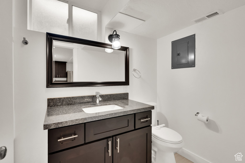 Bathroom featuring electric panel, toilet, vanity, and baseboards