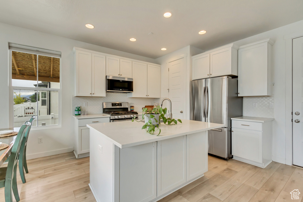 Kitchen featuring appliances with stainless steel finishes, light countertops, light wood-style flooring, tasteful backsplash, and white cabinetry