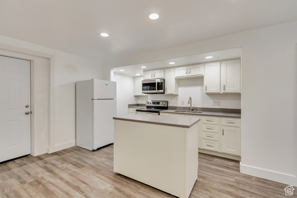 Kitchen featuring stainless steel appliances, a sink, light wood finished floors, a center island, and baseboards