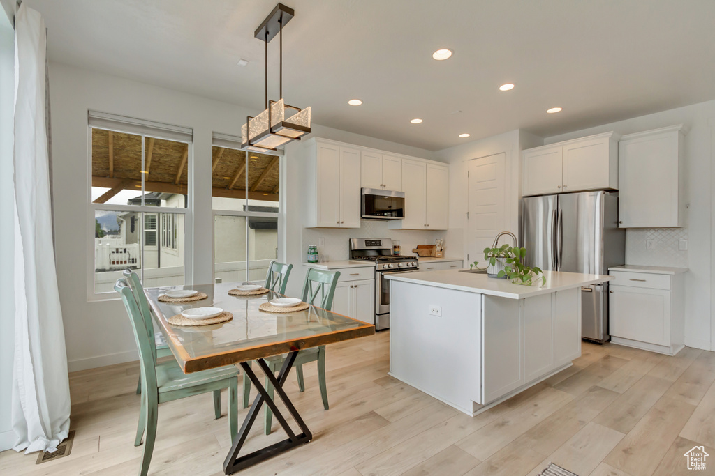 Kitchen with appliances with stainless steel finishes, light countertops, white cabinets, hanging light fixtures, and recessed lighting