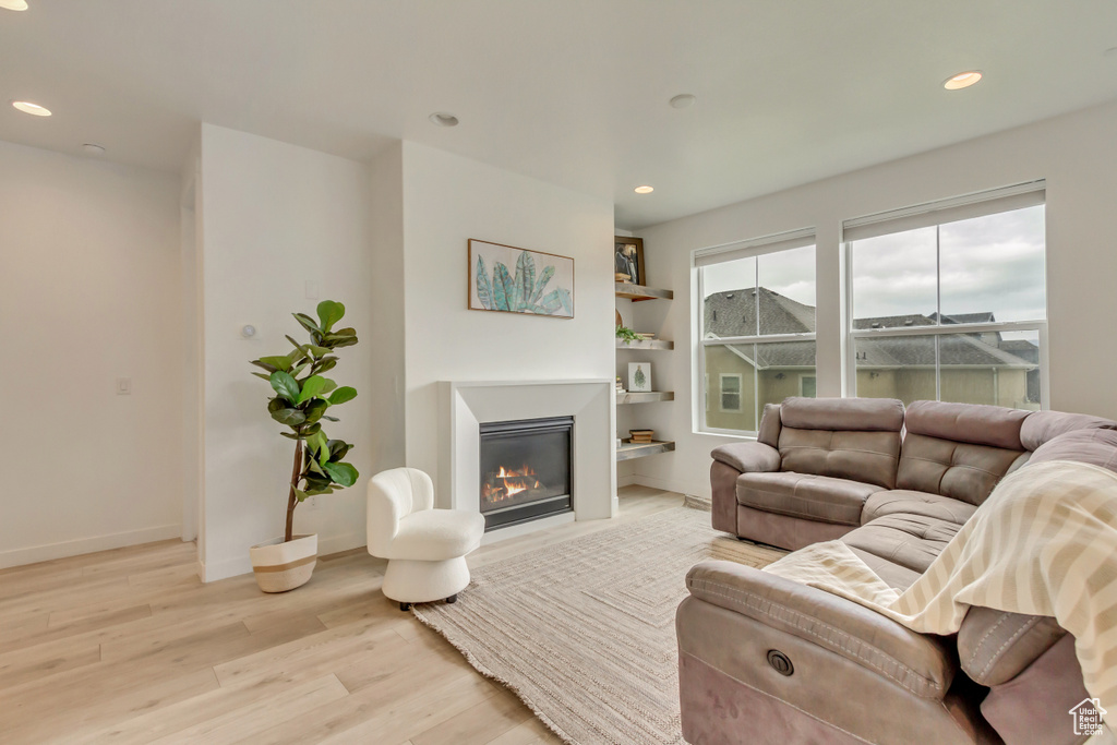 Living area featuring light wood finished floors, a glass covered fireplace, recessed lighting, and baseboards